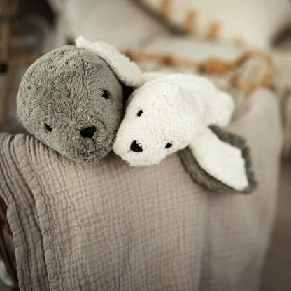 Two plush toy seals, one gray and one white, on a textured blanket with a blurred background.