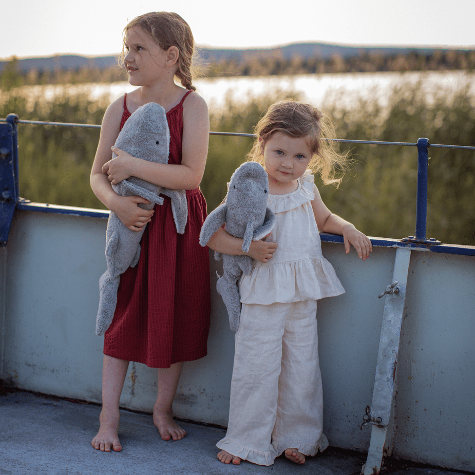 Two young girls holding plush shark toys on a boat with a scenic background