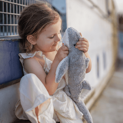 Child holding a shark plush toy against a wall.