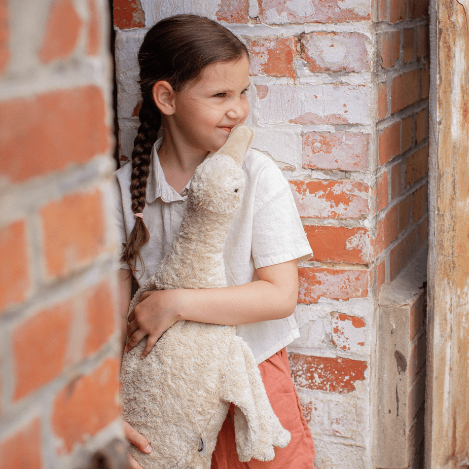 Young girl holding a stuffed goose against a brick wall