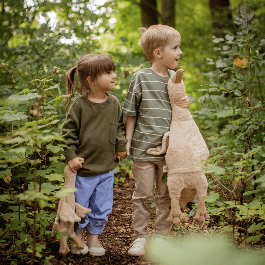 Two children in a forest each holding a stuffed goose