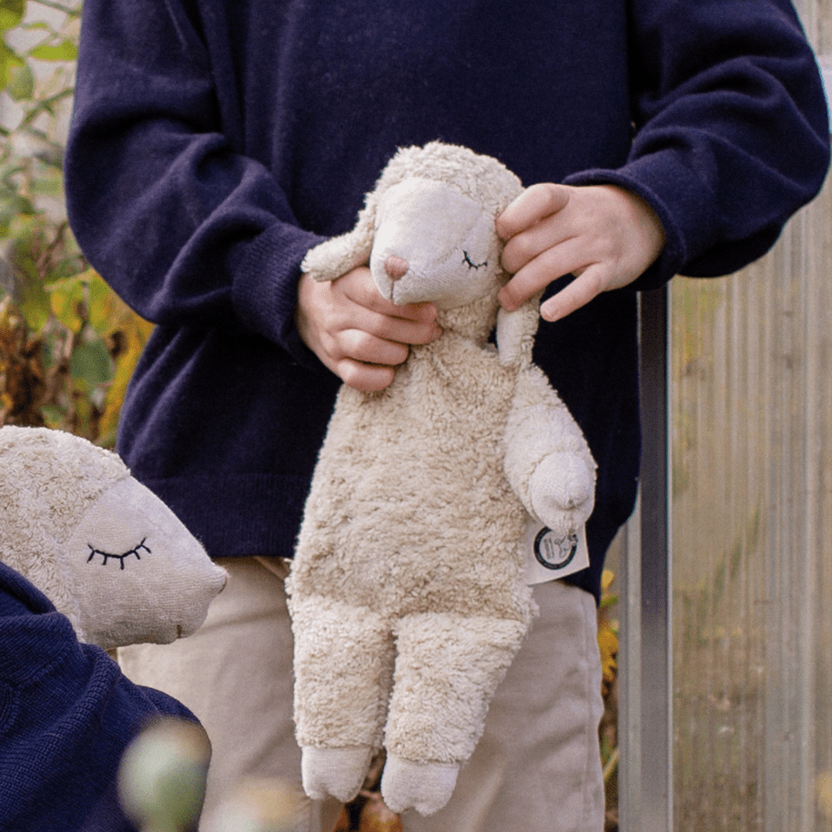 Child holding a plush sheep toy outdoors