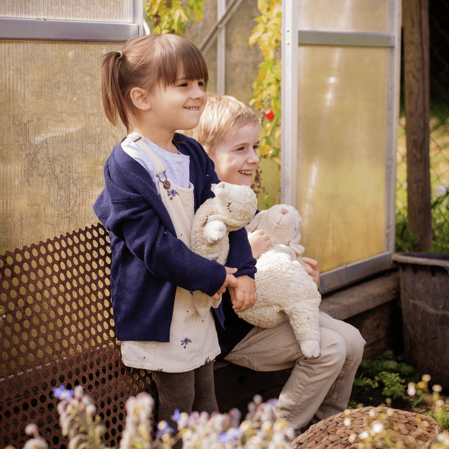 Two children holding cuddly sheep plushies in a garden setting