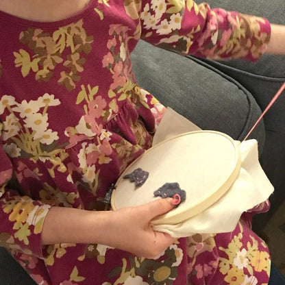 Child sitting on a couch working with an embroidery hoop and pink thread.