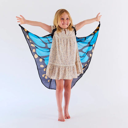 Child wearing a floral dress, holding onto edges of blue butterfly dress up wings