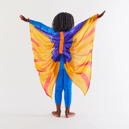 Child wearing an all blue outfit, facing away from the camera to display purple, yellow, and orange pterodactyl wings
