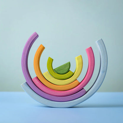 A set of pastel-colored wooden arch blocks arranged in a semi-circular stack on a light blue surface against a pale blue background.