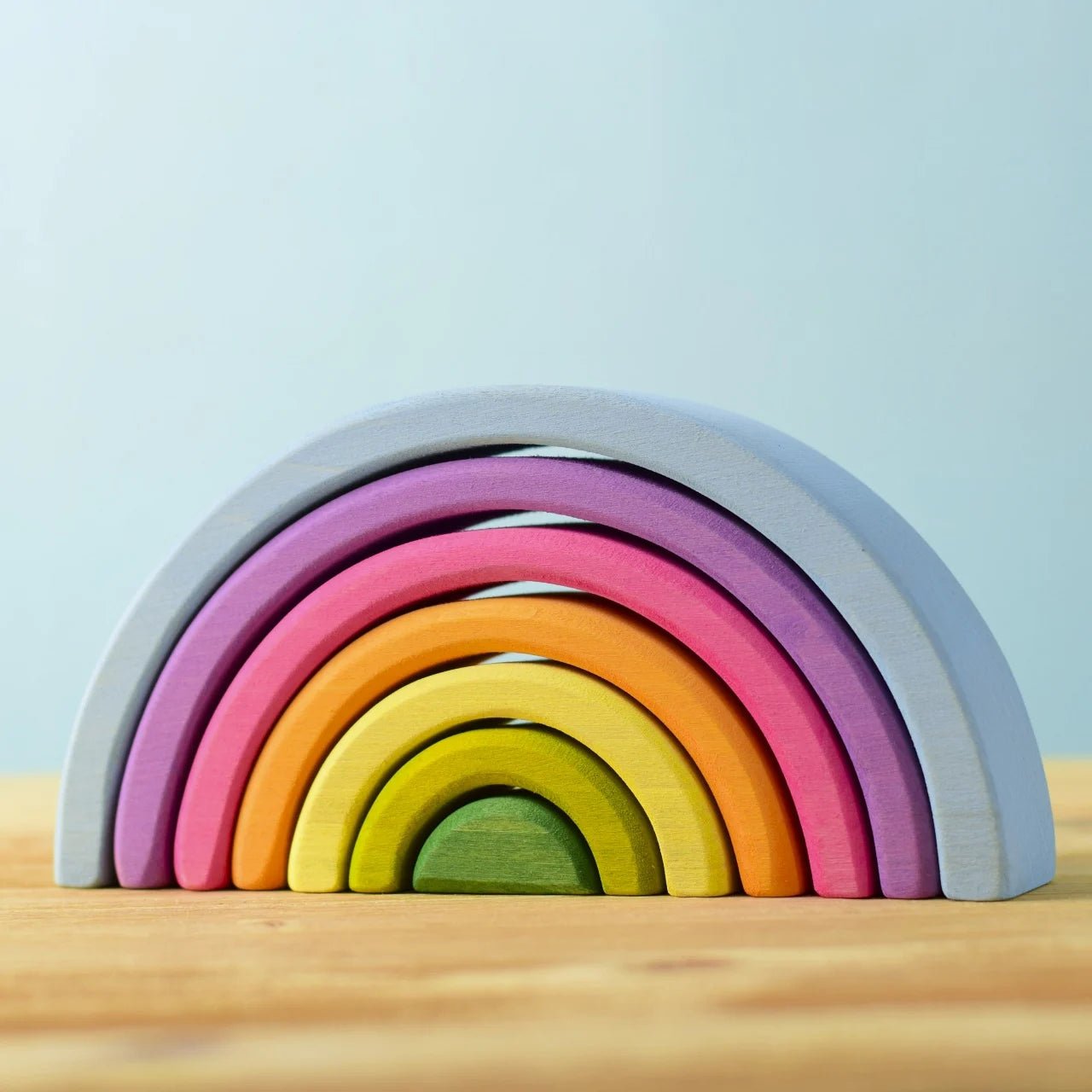 Stackable rainbow arcs on a wooden surface on a light blue background