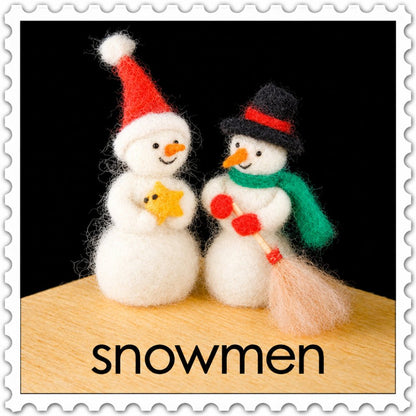 Two felted snowmen, one with a red Santa hat, the other with a black top hat on a wooden surface on black background