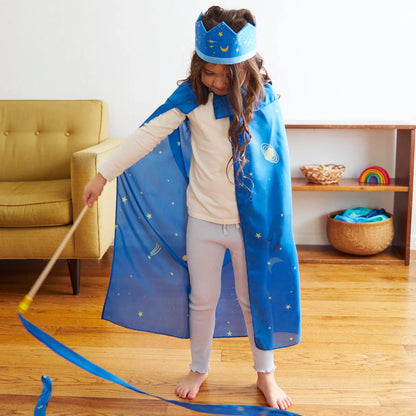 Child in a blue cape and crown playing with a wand in a room.