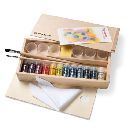 Wooden art supply set with paint bottles, brushes, and a towel on a white background