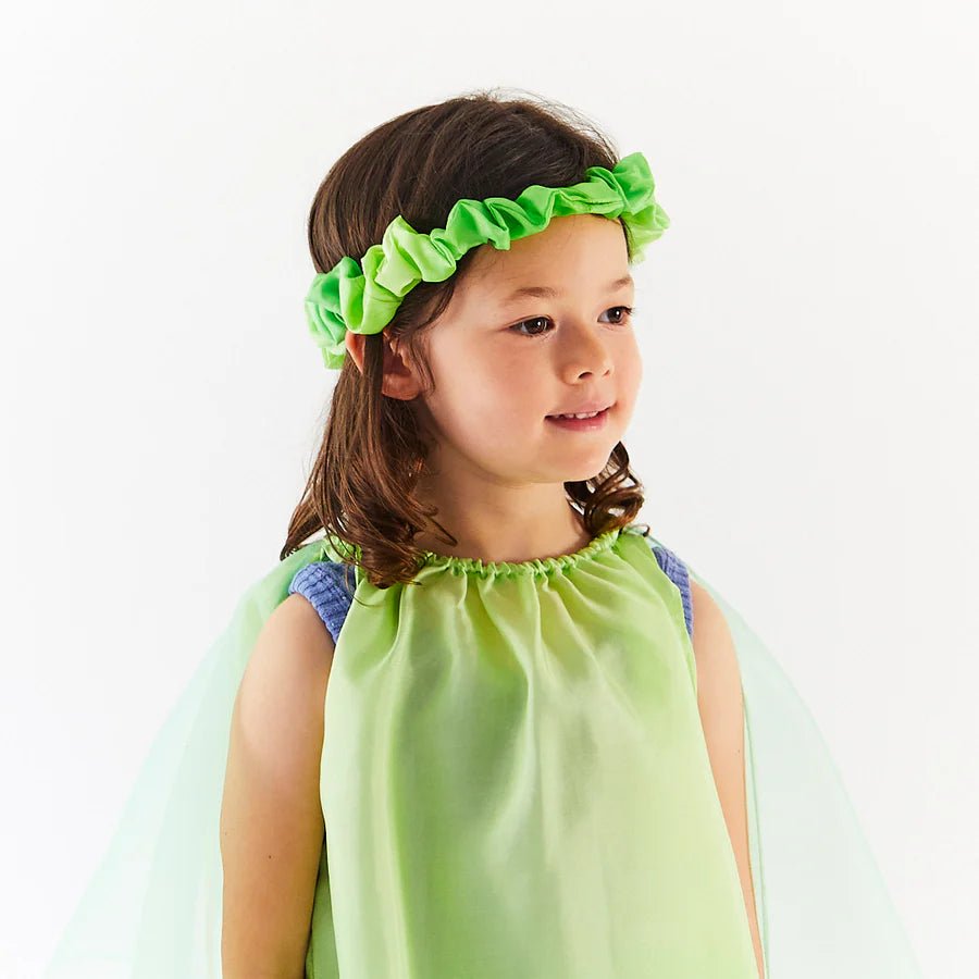 Child wearing a green dress and headband against a white background