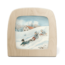 Silhouette of three children sledding down a snowy hill, with house in the background