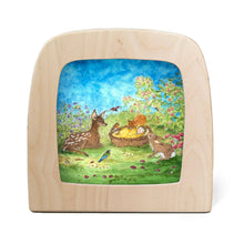 Silhouette of a baby sleeping in a wicker basket, watched over by deer, rabbits, and birds