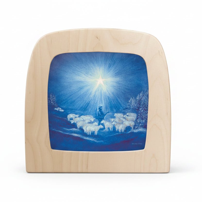 Wooden plaque with a painted scene of a shepherd and sheep under a bright star on a blue sky.