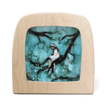 Silhouette with a woman sitting on a branch against a turquoise background, framed by a light wood border.