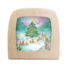 A square wooden picture frame with rounded corners, featuring a colorful painted winter forest scene with a Christmas tree, animals, and a snowy ground, shown on a plain white background.