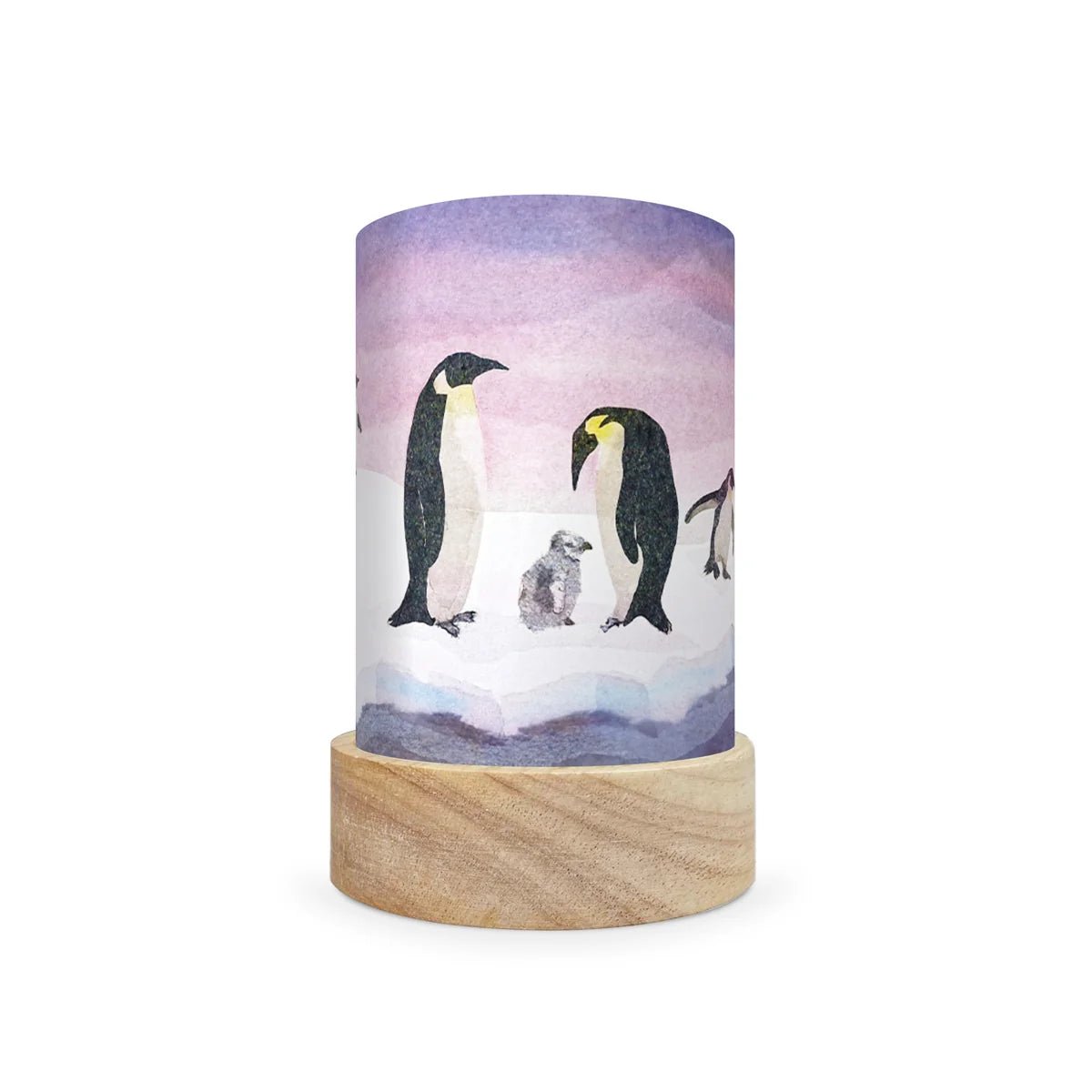 A cylindrical decorative lamp shade with a light wood base and a printed wrap featuring penguins on ice under a purple sky, shown on a white background.