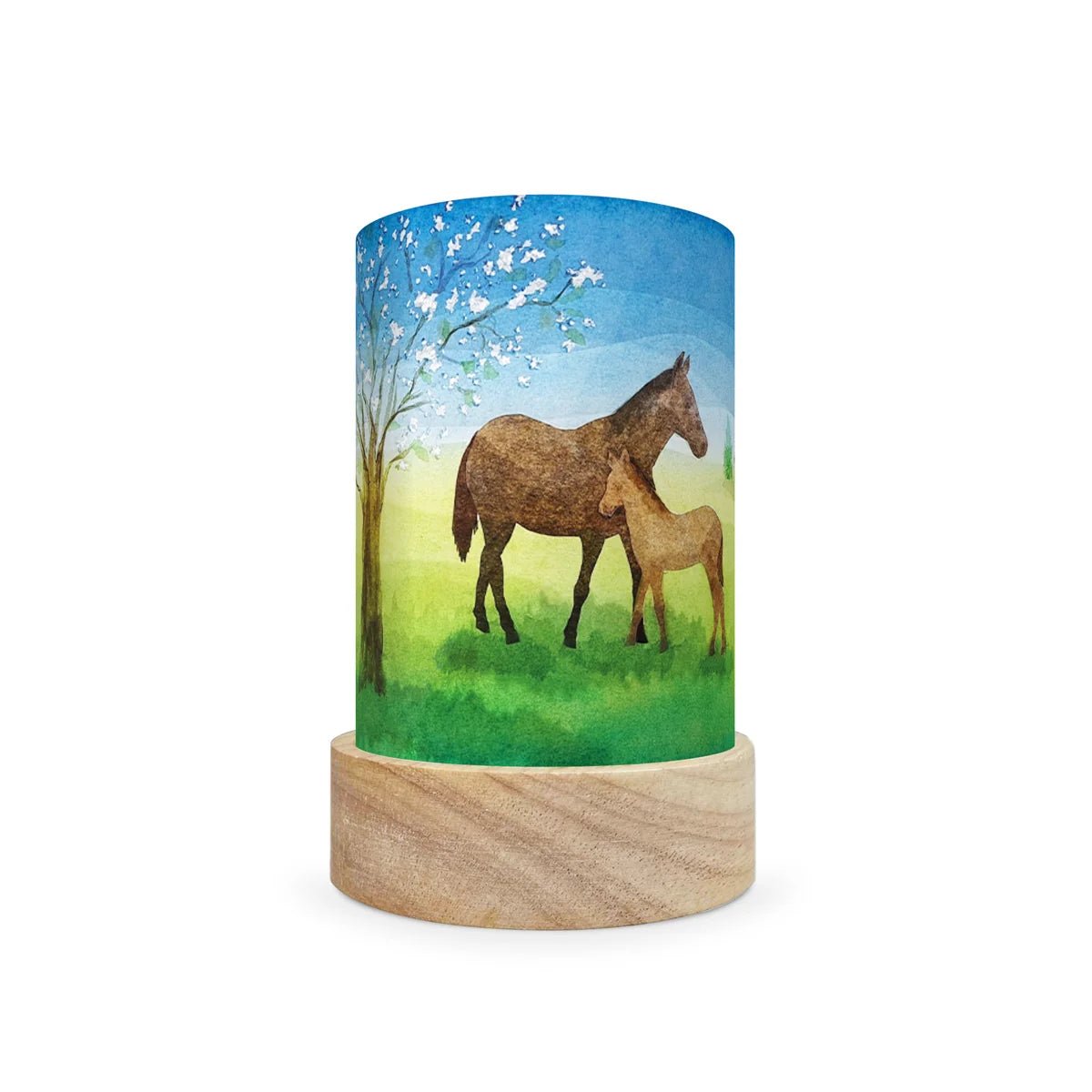 A cylindrical decorative lamp shade with a light natural wood base and a printed wraparound cylinder featuring a painted scene of a brown horse and foal under a blue sky with white blossoms.