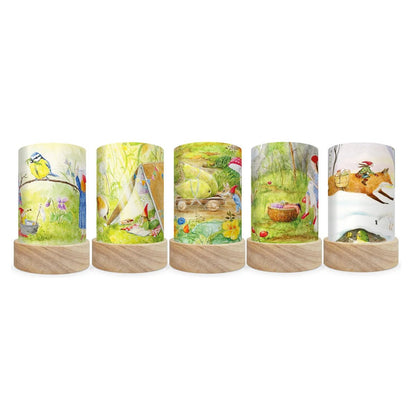 Five decorative cylindrical lamp shades with light wood bases, each featuring a different whimsical watercolor nature illustration on the wrap-around surface, set against a plain white background.