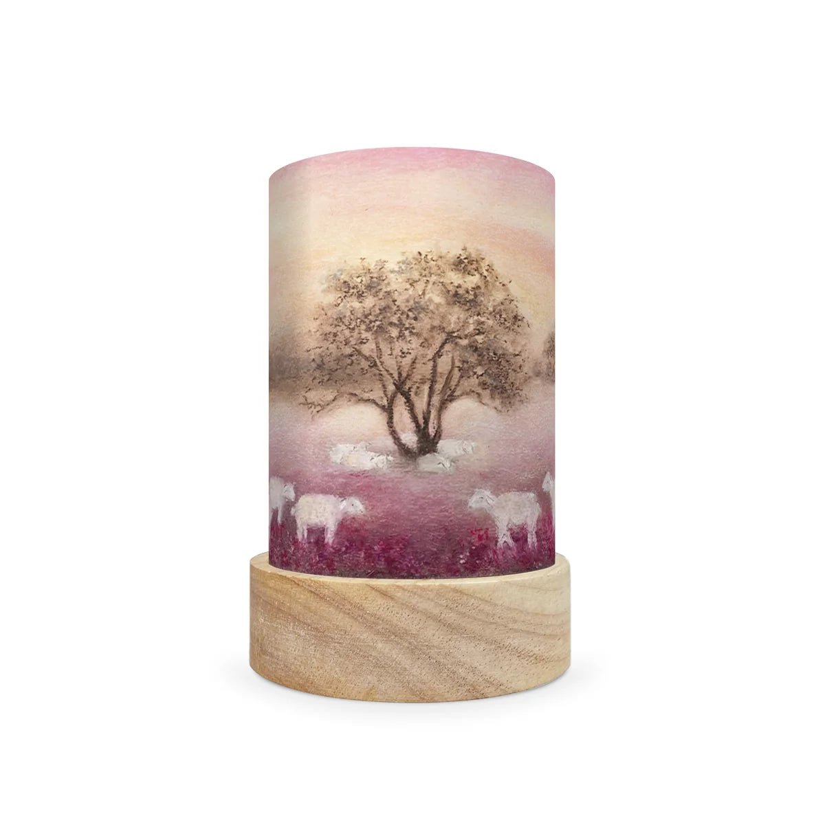 A cylindrical decorative lamp shade with a light wood base and a printed cylinder body featuring a scenic landscape of a tree and sheep in a field under a pink sky.