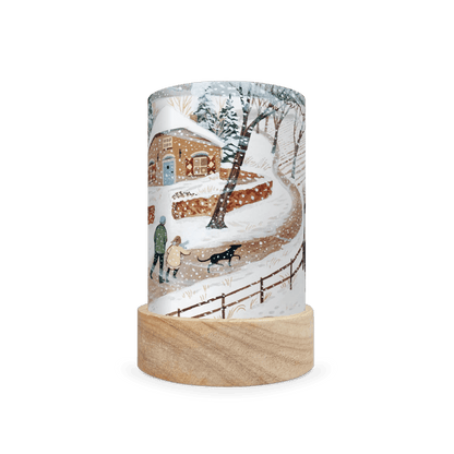 Decorative lamp depicting a scene of two people walking a dog in the snow on a white background