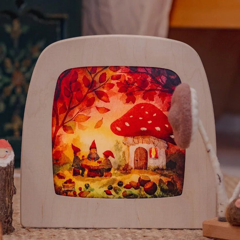 Decorative silhouette lamp with a fairy tale scene surrounded by small figurines on a textured surface.