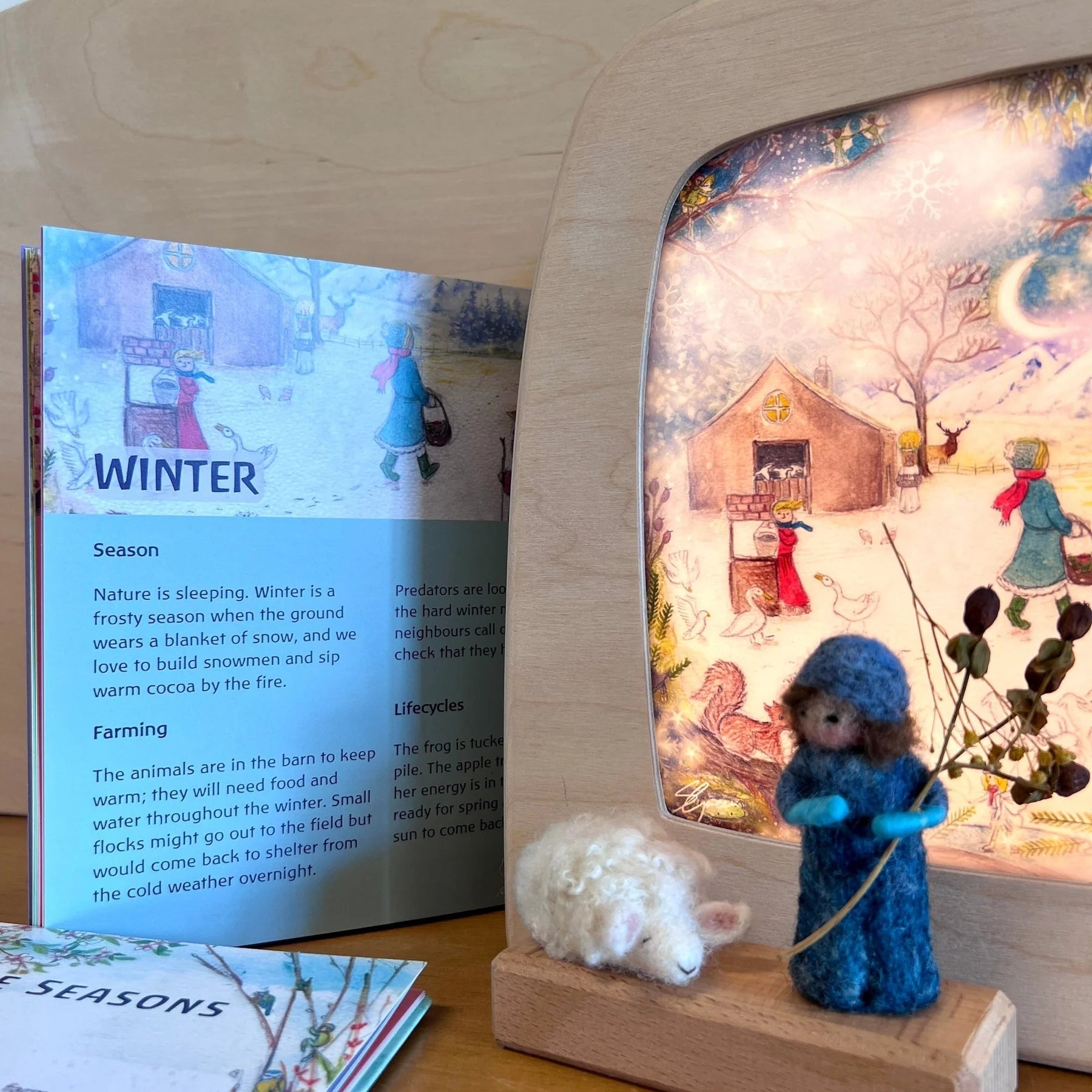Through the Seasons book turned to the winter page, next to Toverlux lamp with winter silhouette