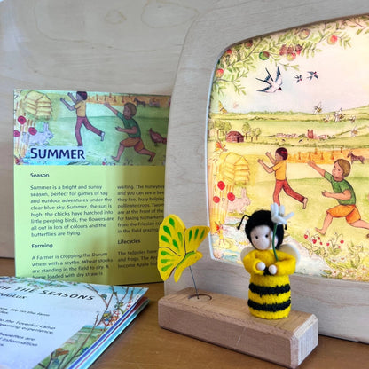 Children's book about seasons with a bee figurine and decorative elements on a wooden surface.