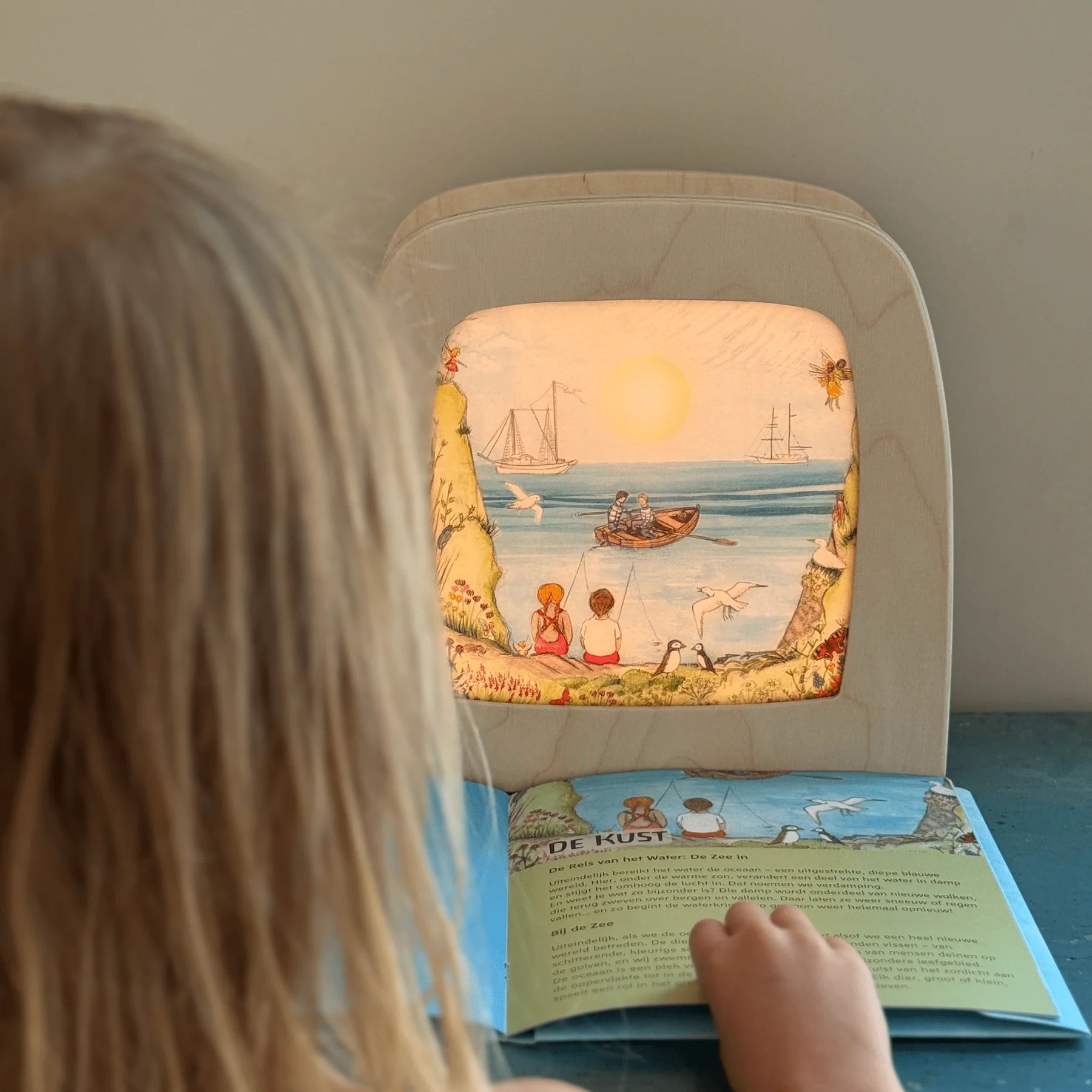 Child looking at a book with a colorful illustration of a beach scene.
