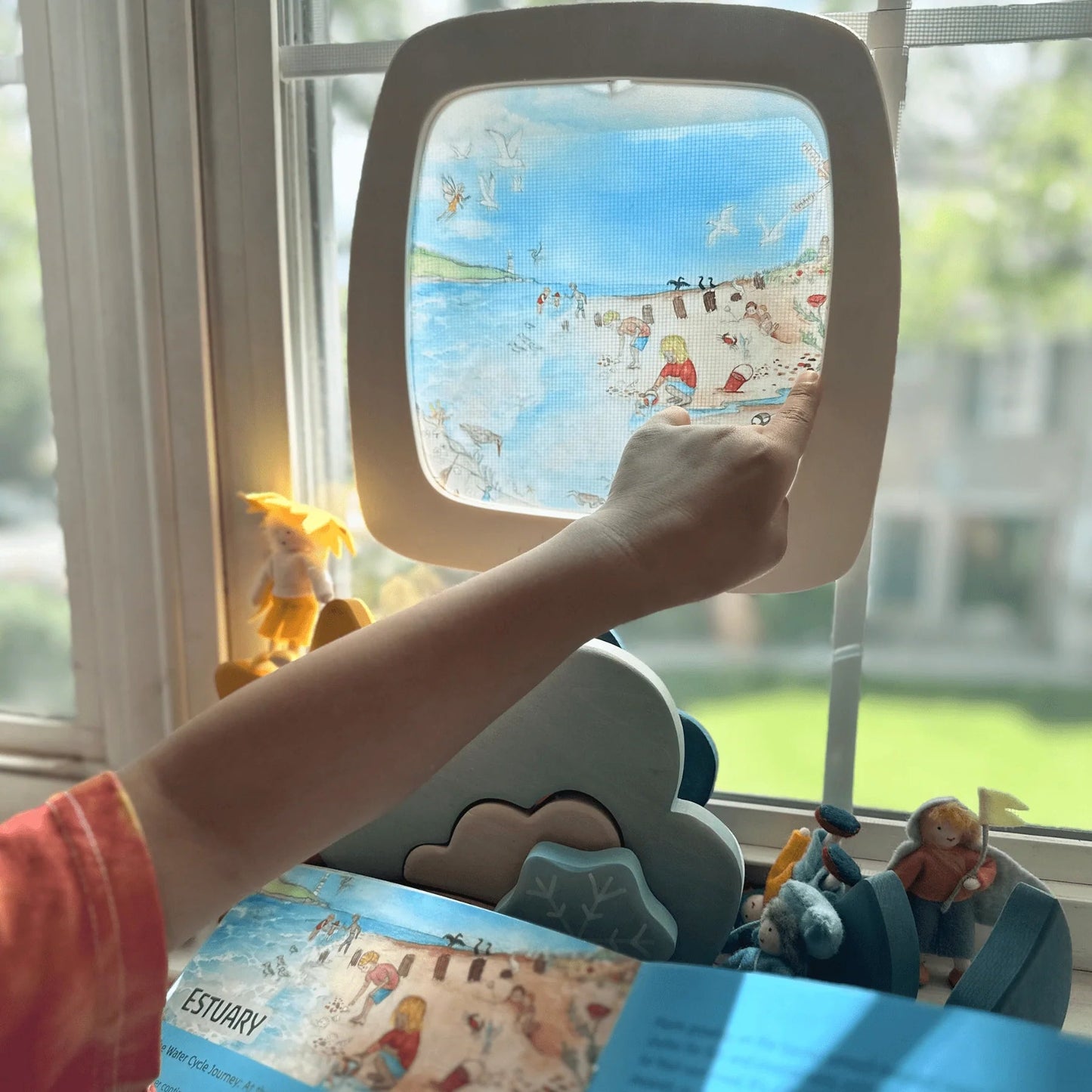 Child pointing to silhouette of the seaside. Frame is held up against the window to showcase the natural light shining through from outside.