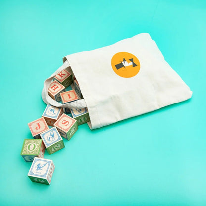 Colorful wooden blocks spilling out of a white drawstring bag with a logo on a teal background
