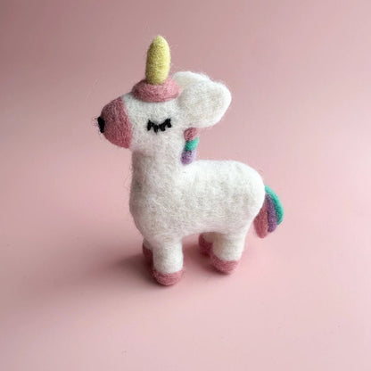 White felted unicorn with pink snout and hooves, with pink, teal, and purple tail on a pink background