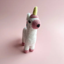 Stuffed unicorn toy with a pink snout and yellow horn on a pink background