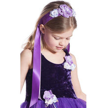 A young girl wearing a purple flower girl costume dress with a matching purple headband adorned with purple and white fabric flowers, looking down against a white background.