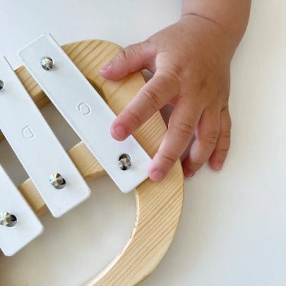 Child's hand playing a small wooden xylophone on a white surface