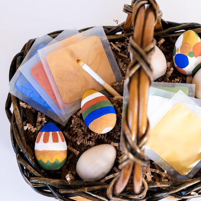 Basket with colorful Easter eggs, paint, and paint brush on a white background