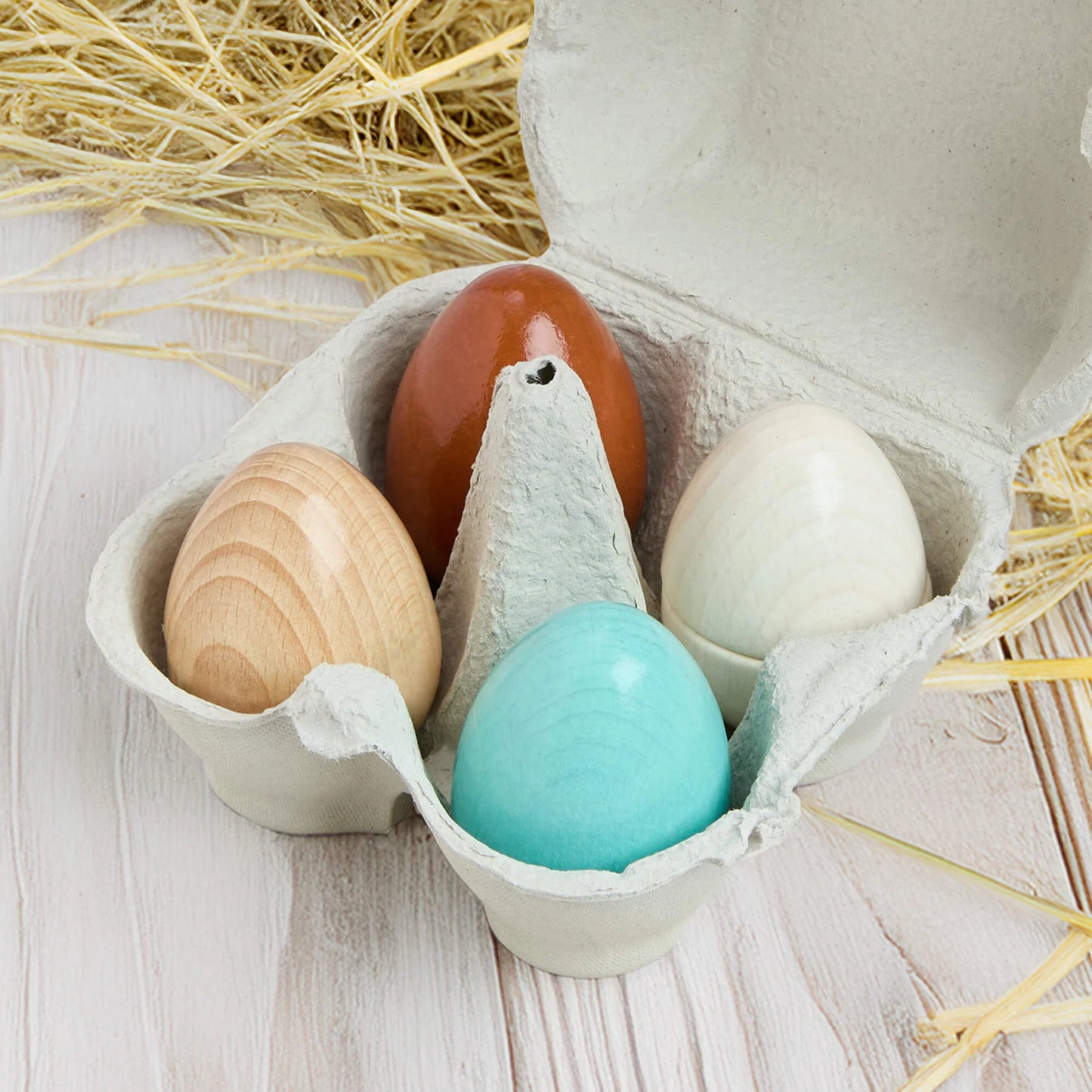 Colorful wooden eggs in a carton on a wooden surface with straw.