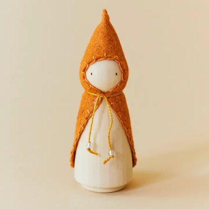 Wooden gnome figure with an orange hood and coat on a beige background