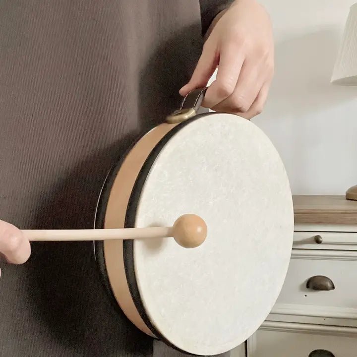 Person playing a small drum with a wooden stick in a room setting.