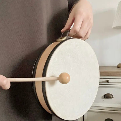Person playing a small drum with a wooden stick in a room setting.