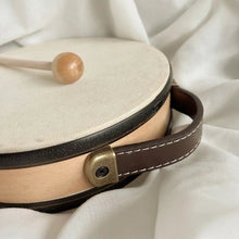 Small round drum with a wooden mallet on a white fabric background