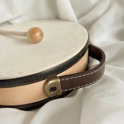 Small round drum with a wooden mallet on a white fabric background