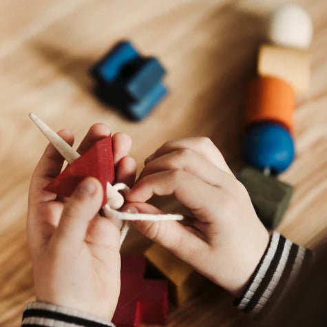 Child threading blocks using wooden needle