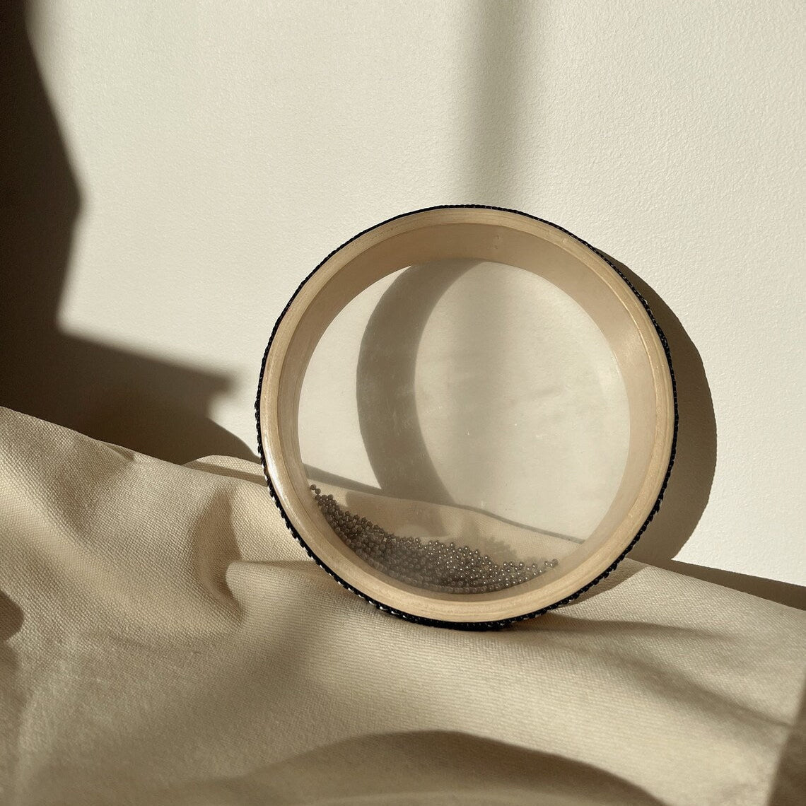 Wooden drum with metal beads inside leaning against a wall with soft shadows