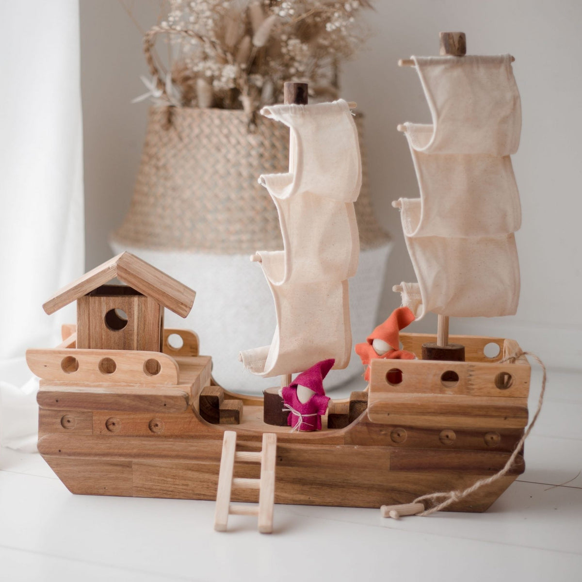 Wooden toy pirate ship with two wooden people on a white surface.
